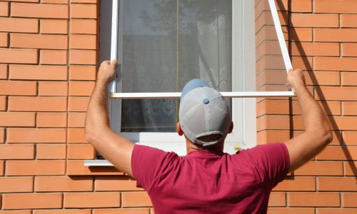 Contractor installing mosquito wire screen on house window to protect from insects. Mosquito wire screen installation.
